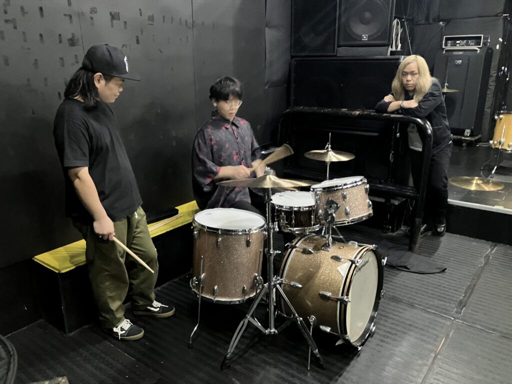 ドラムセットを中心に語りあう男性3人